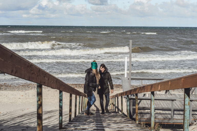 a young couple in love spending weekends on the coast of the cold Baltic sea, sandy beach, warm jackets, family weekend man and woman running on the beach.