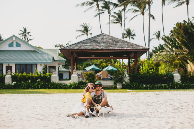 young stylish hipster couple in love walking playing dog puppy jack russell, tropical beach, cool outfit, romantic mood, having fun, sunny, man woman together, horizontal, vacation, house home villa